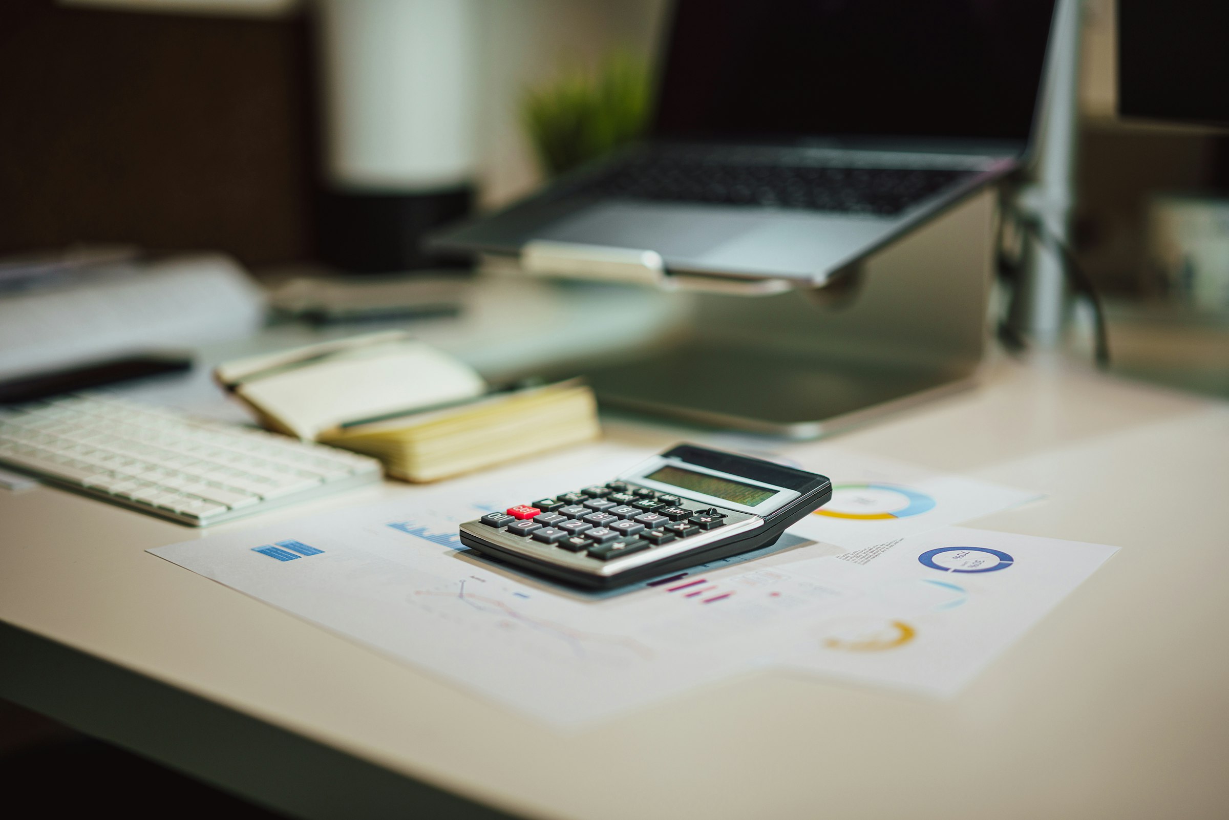 Calculator resting on printed financial charts beside a laptop