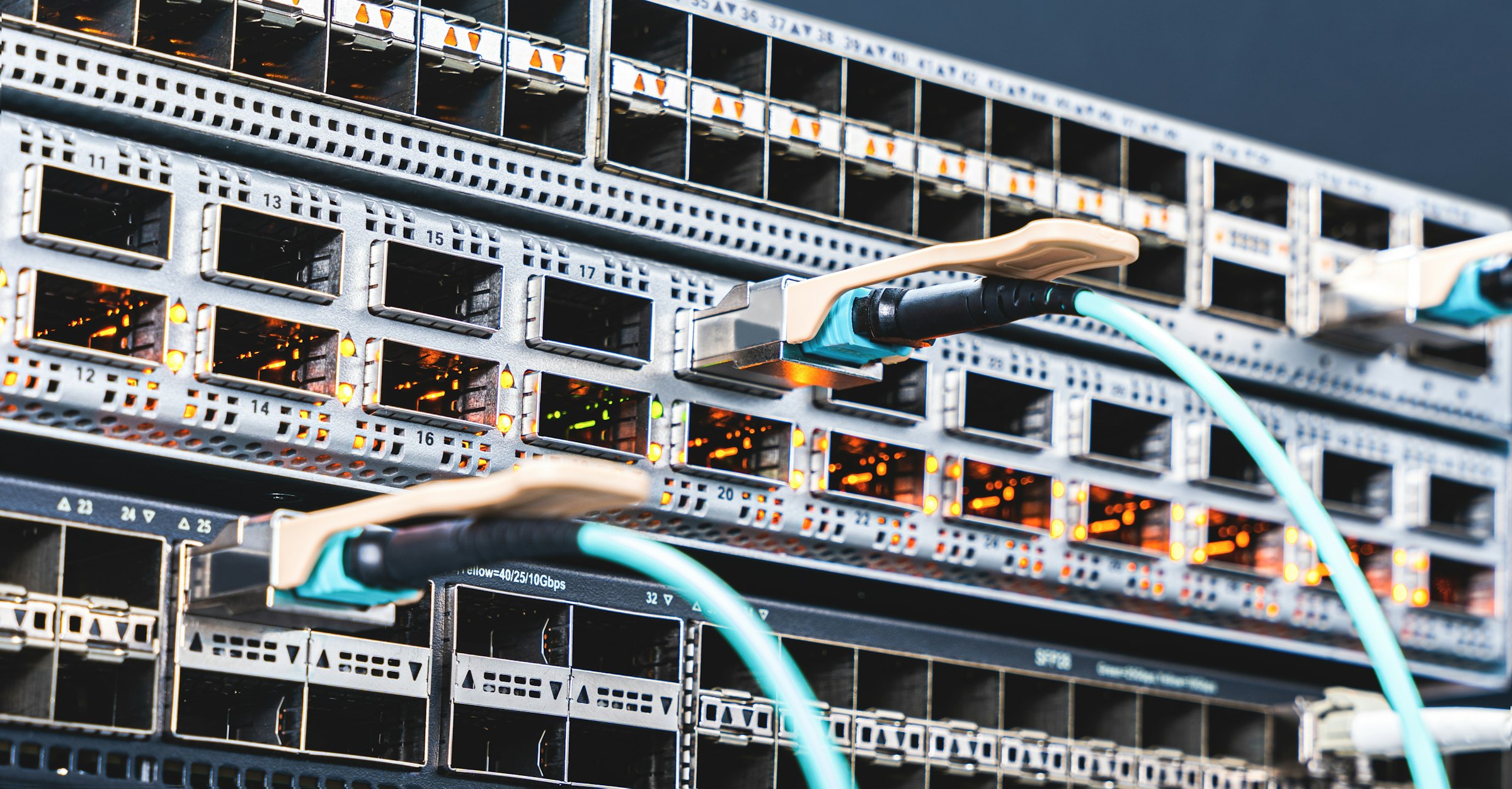 Network switches with teal fiber-optic cables in a server rack